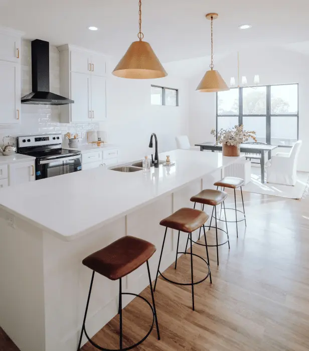 A modern kitchen with white cabinets, a large island with bar stools, and two pendant lights