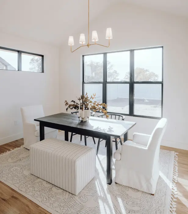 A bright dining room with a dark table, white chairs, a striped bench, a rug, and a gold chandelier